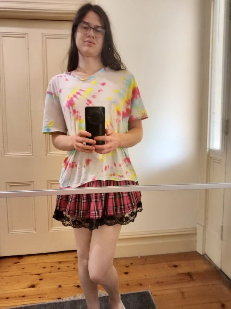 white tie-dye tee nearing threadbare, and a pink miniskirt it doesnt quite go with. there's a doorway behind me which my head reaches the top of, which is definitely an accurate representation of my height and not a trick of perspective.