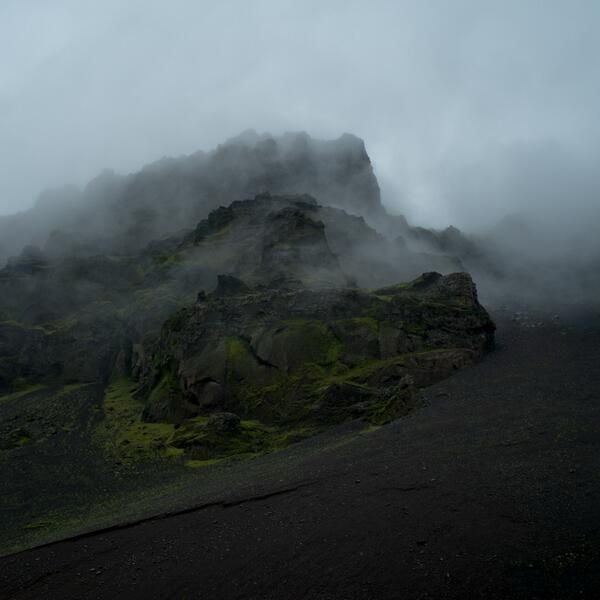 A photo of a foggy Icelandic mountainside featuring craggy rocks, lichen and volcanic scree