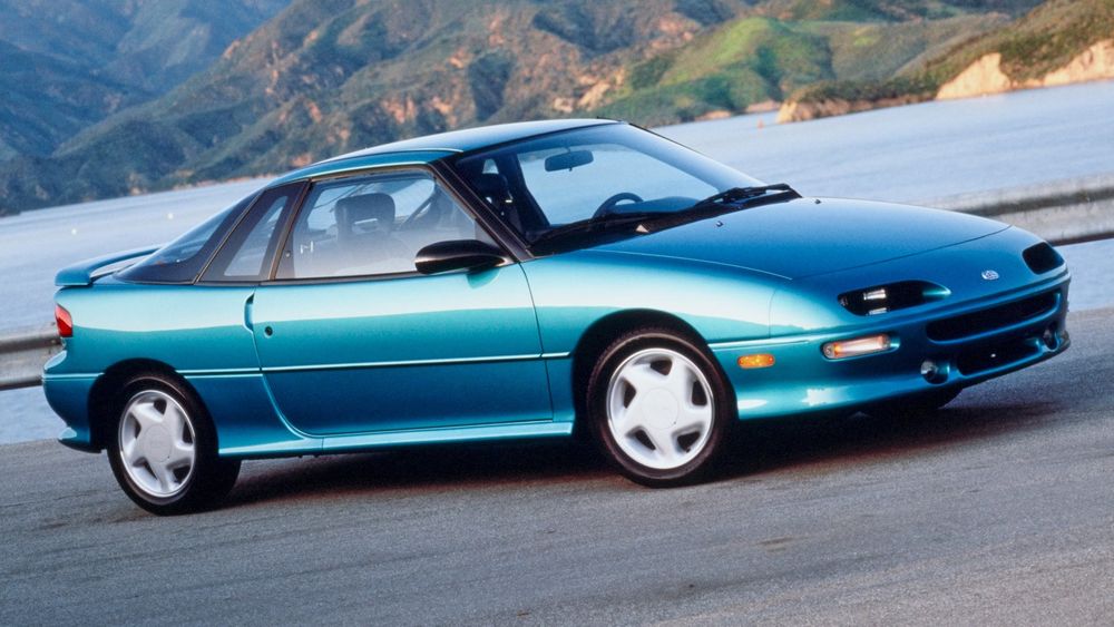 Blue Geo Storm car in front of a lake with steep shores across the water.