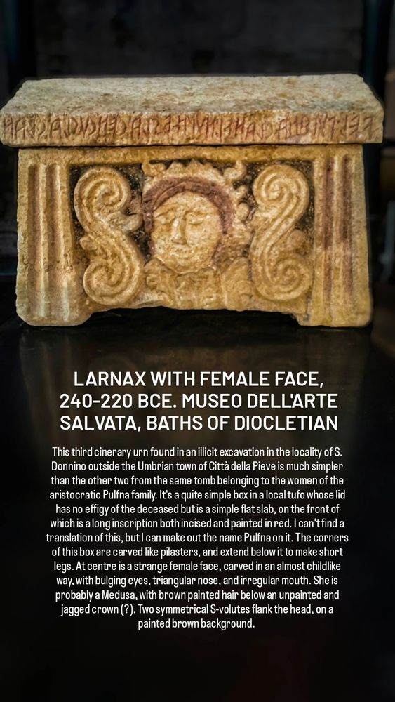 LARNAX WITH FEMALE FACE, 240-220 BCE. MUSEO DELL'ARTE SALVATA, BATHS OF DIOCLETIAN

This third cinerary urn found in an illicit excavation in the locality of S. Donnino outside the Umbrian town of Città della Pieve is much simpler than the other two from the same tomb belonging to the women of the aristocratic Pulfna family. It's a quite simple box in a local tufo whose lid has no effigy of the deceased but is a simple flat slab, on the front of which is a long inscription both incised and painted in red. I can't find a translation of this, but I can make out the name Pulfna on it. The corners of this box are carved like pilasters, and extend below it to make short legs. At centre is a strange female face, carved in an almost childlike way, with bulging eyes, triangular nose, and irregular mouth. She is probably a Medusa, with brown painted hair below an unpainted and jagged crown (?). Two symmetrical S-volutes flank the head, on a painted brown background. 