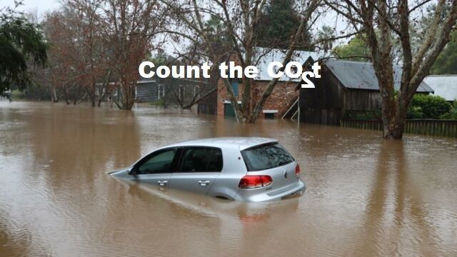Photo of a half submerged car on a suburban street the brown flood water stretches from side to side turning  the road into a river.
Superimposed on the image the words "Count the cost" where the "s" of "cost" is made made by a figure 2 flipped horizontally so it reads as an "s" so the message is count the CO2 (the formula for carbon dioxide) and count the cost of the impact of climate change induced by global warming. 