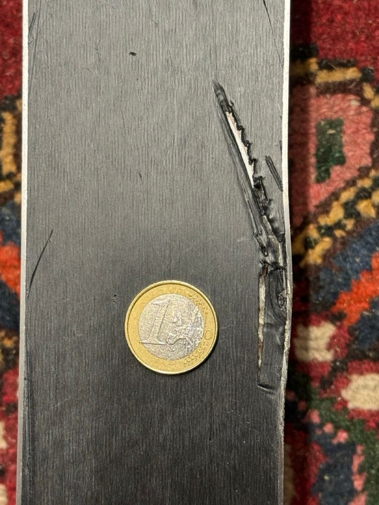 Ausgerissene Kante bei einem Ski, Draufsicht auf die schadhafte Stelle mit einer Euro-Münze als Größenvergleich.