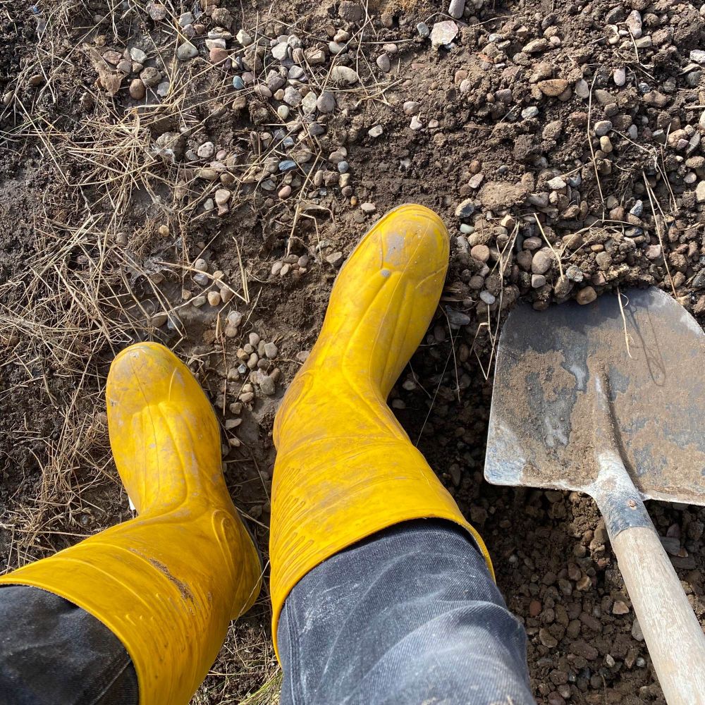 Photo of a shovel and my feet in a pair of yellow rubber boots.