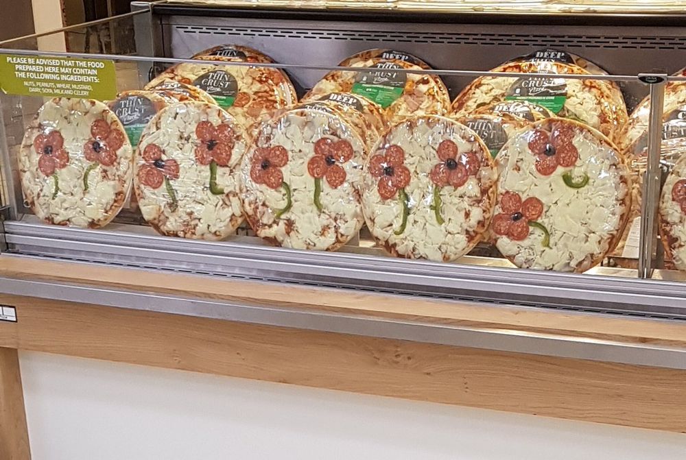 a row of cheese pizzas with pepperonis in the shape of remembrance poppies, an olive in the centre and a green pepper stem.