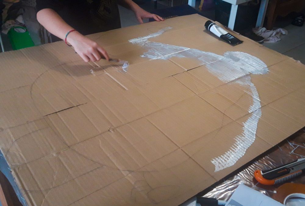 Crayonné d'une silhouette de Baymax des Nouveaux Héros, sur carton à plat
Une main d'enfant est en train de passer la première couche de peinture blanche