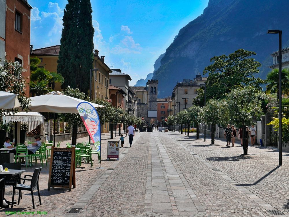 Taken on Viale Roma looking South towards the old town centre. A broad pedestrianised boulevard with shops and restaurants. To the right tall cliffs define the edge of the town as they swoop down to Lake Garda.