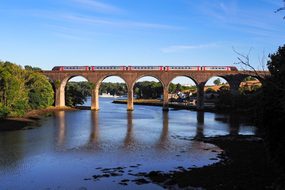 View on the same viaduct, but this time from the side. Lake in the foreground, behind the viaduct the old houses from earlier that day. A silver-red Voyager crosses the bridge in the evening light.
