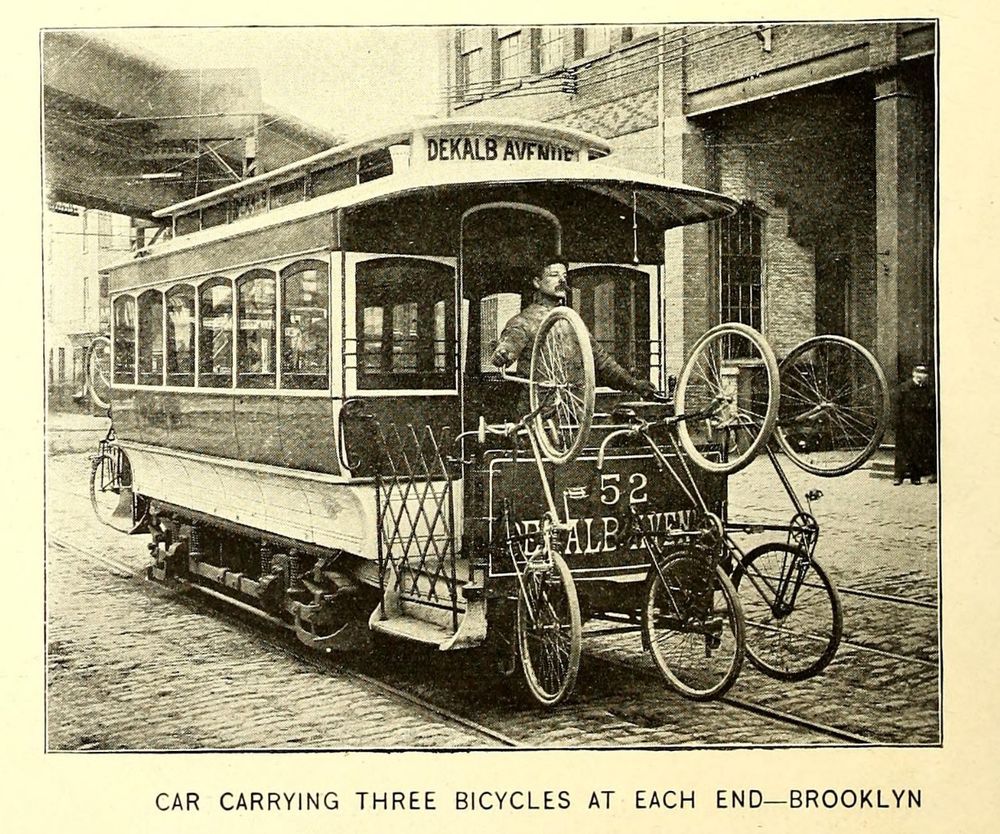 Ventage photo of an old streetcar with three safety bicycles hanging off one end and more on the back. Caption: “Car carrying three bicycles at each end - Brooklyn”