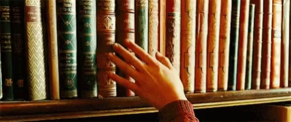 a person is reaching for a book on a bookshelf in a library .