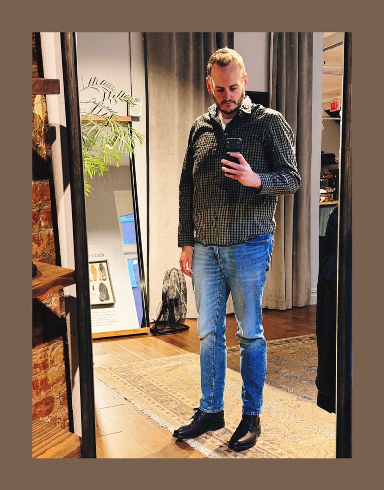 David wearing jeans, a green and blue checked long-sleeve button-down shirt, and dark brown leather boots