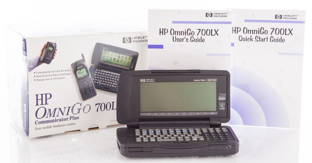 A 90's catalog image for the HP Omnigo 700LX. The device itself is a chubby rubberpized pebble with a CSTN display; the box (left) shows there's a recess for the included Nokia phone, allowing true wireless communication; the thick user's guide and the slim quick start guide appear right.