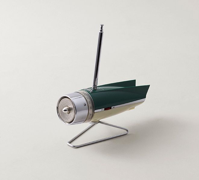 A radio that combines the design language of old American muscle cars and the spacerace. The top is forest green with tailfins, the bottom is ivory white, and the front is shining silver, on a silver stand. Up top we find a single antenna, a red power/volume dial, and you turn the 'intake" of the rocket to change the stations (the tuning display is immediately behind the engine, incoporated into the body).