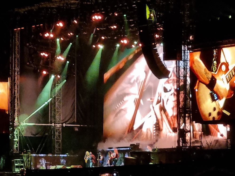A picture of Iron Maiden on stage. However, you see mostly the screen with Eddy as pilot, and the band as tiny people in front.