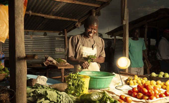 Smiling African woman preparing foot next to solar-powered light.