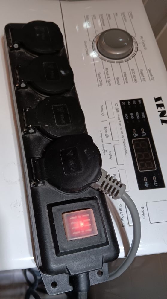 Musta, ulos tarkoitettu jatkojohto pyykkikoneen päällä.