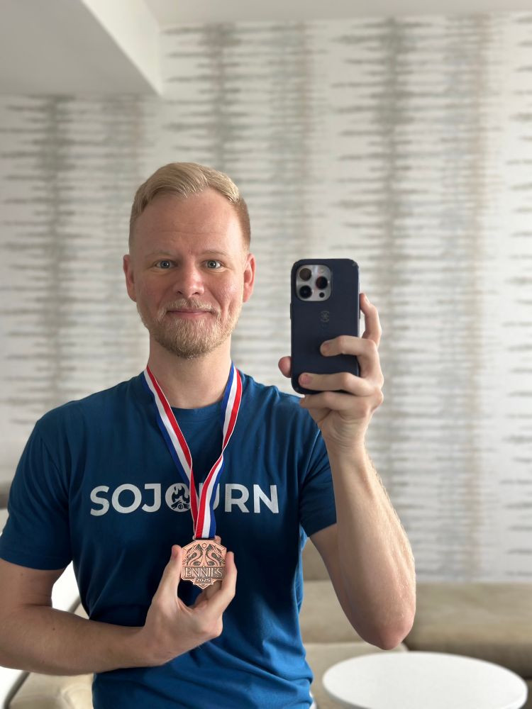 Handsome bearded blond in a Sojourn shirt smiling with his ENNIE Award medal