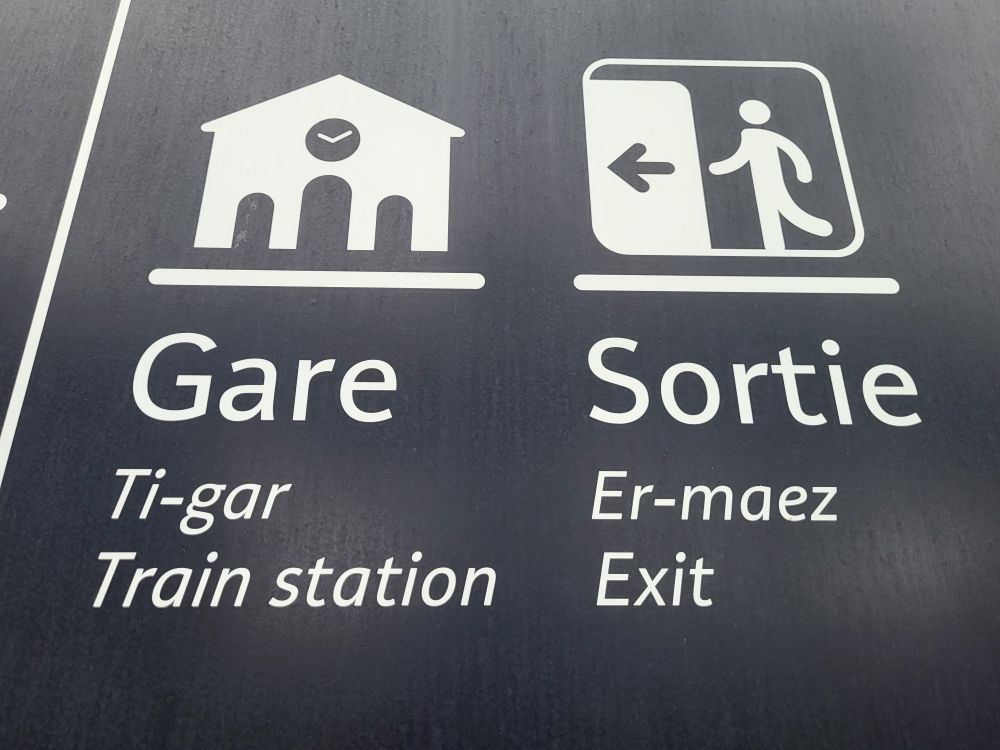 A trilingual sign showing Gare, ti-gar and Train station in French Breton and English