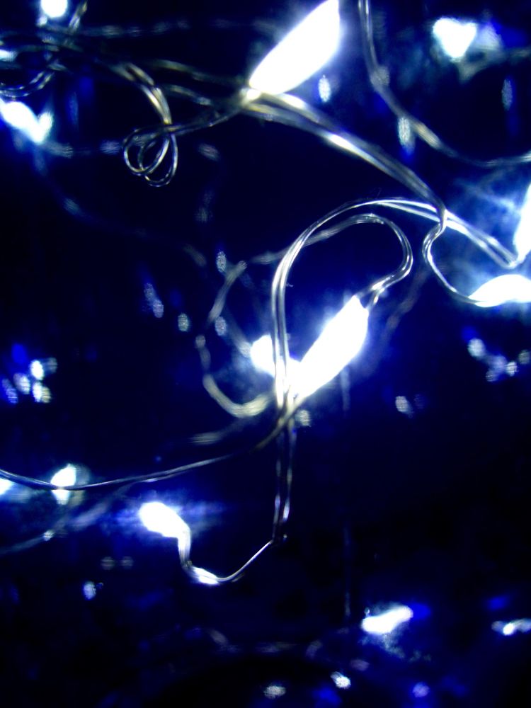 Nahaufnahme einer Lichterkette mit Mini-LEDs, die in einer dunkelblauen Glasflasche stecken.