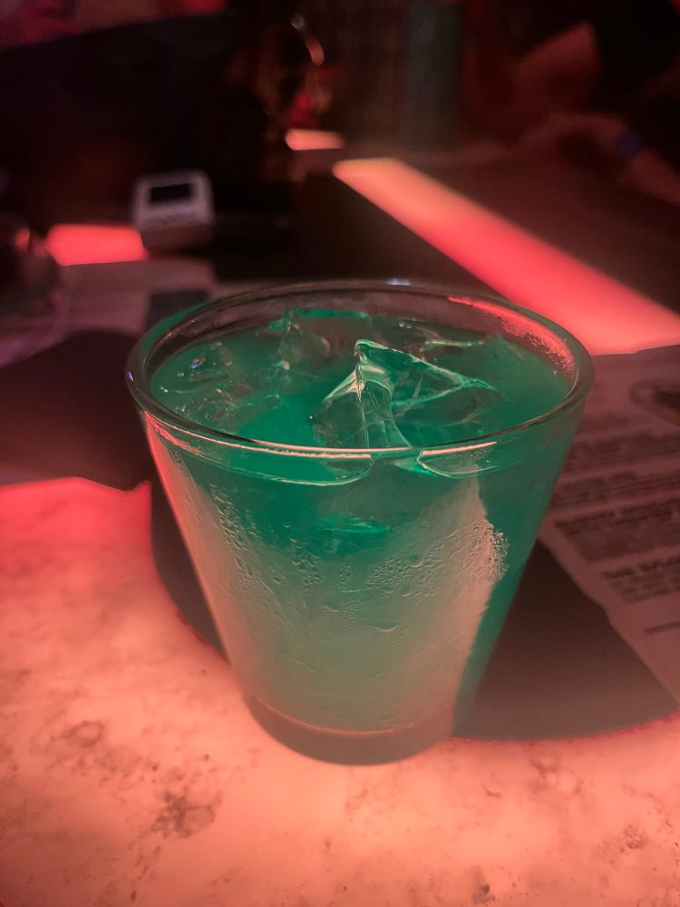 A greenish drink with ice in a angled cup on a bar called Oga’s Cantina.