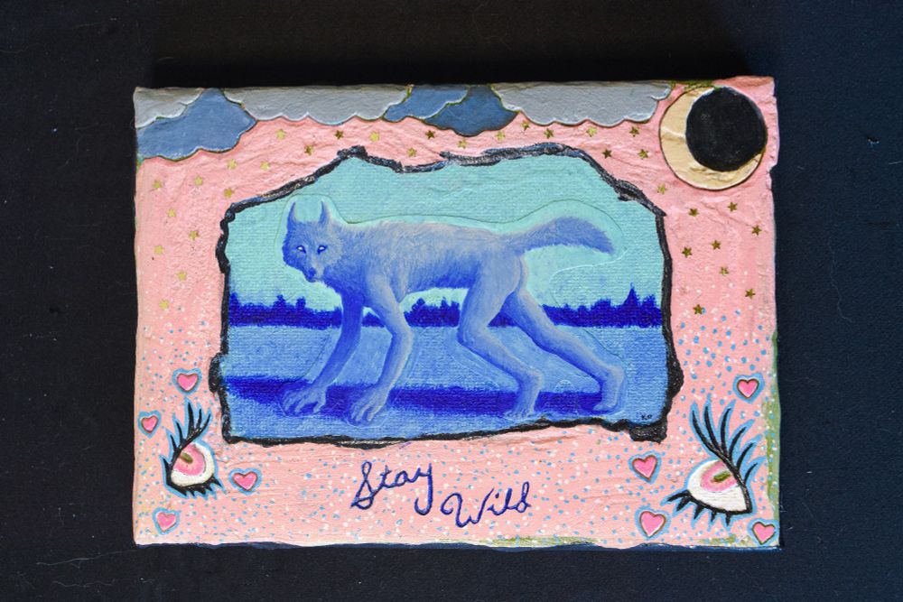An acrylic painting sitting on a black background. The painting features a blue werewolf with a nondescript landscape behind it. The scene is surrounded by a rough, pink border. Two eyes with pink irises, surrounded by pink hearts, are carved in the lower corners of the painting. At the top of the pink border are clouds and a moon, also carved into the painting. Gold metallic stars appear to fall from the clouds. In the bottom middle of the painting the words "Stay Wild" are carved in blue script. 

#art #blueskyartist #artsky #painting #acrylicpaint #werewolf #fantasyart #experimentalart #experimentalpainting #eyes #moon #clouds #stars #acrylicpainting 