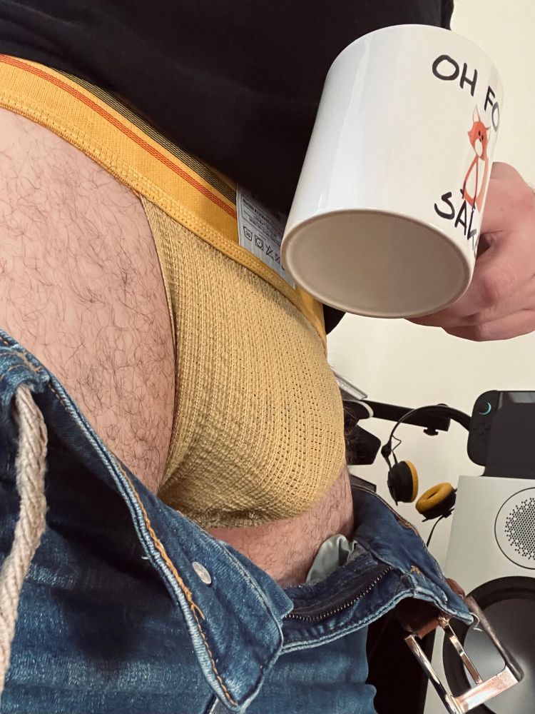 A dick bulge in a yellow sports jock, with a cup of coffee held in the foreground. 