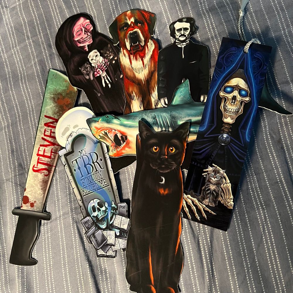 Various bookmarks in a pile; a blood knife with my name on it, a black cat, Death with kitten from Discworld, Jaws, Cujo, Edgar Allen Poe…