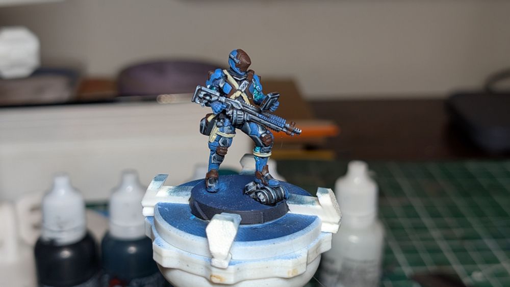 A Kludger from Corvus Belli's Infinity the Game photographed from the front with the bare metal parts painted (Abaddon Black, Incubi Darkness, Thunderhawk Blue, Fenrisian Grey, and Ulthuan Grey). The teal bits of the armour have been blocked in using Aethermatic Blue