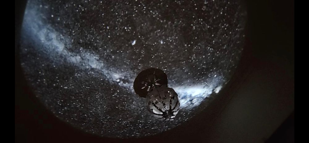 A black and white starry sky projected in a circle over a lampshade hanging from the ceiling. 
