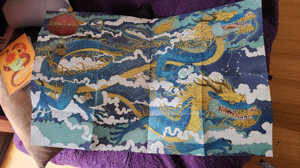 Guide poster for a blue and yellow dragon jigsaw, on a purple tapestry blanket over sn armchair with an orange poetry book to the side.