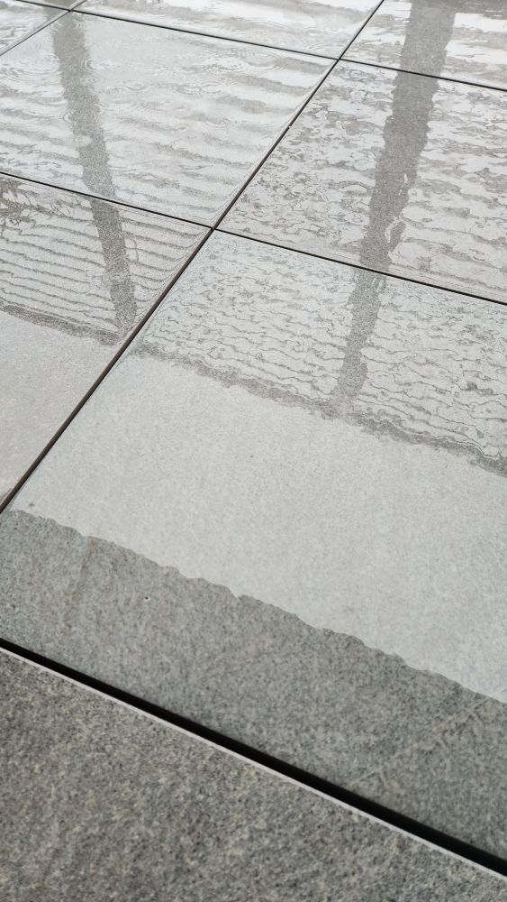 Grey stone tiles with water, raindrops, and dark shadows of railings. 