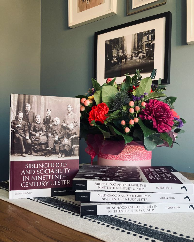 Image of four copies of Siblinghood and Sociability in Nineteenth-Century Ulster by Shannon Devlin and some lovely flowers. 