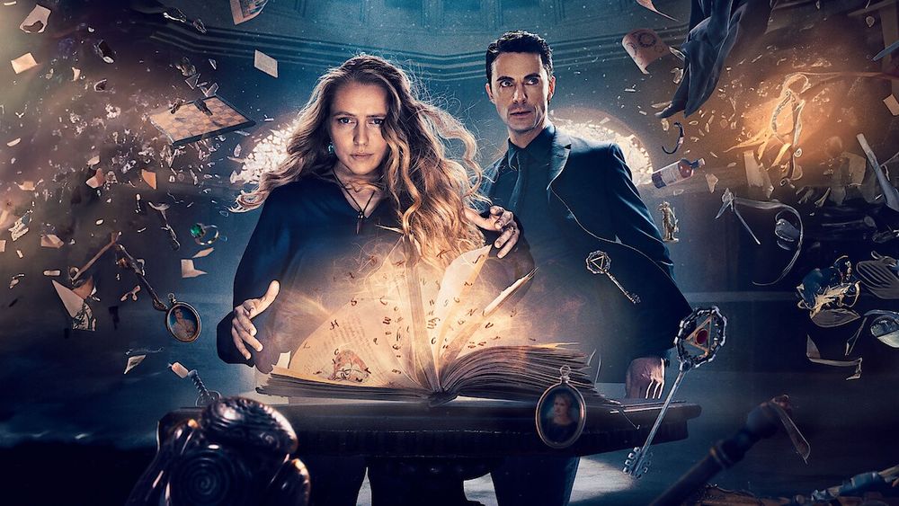 Cover shot for the TV series a Discovery of Witches with a man and women (in dark teal, obvs) reading a spell from a book