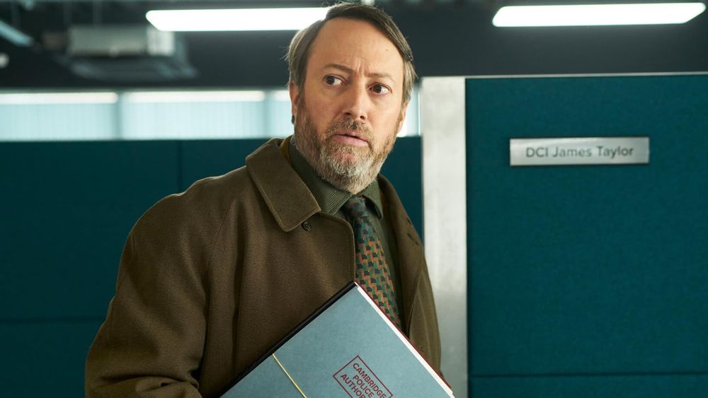 David Mitchell in a darker brown/teal clothes/set set up. 