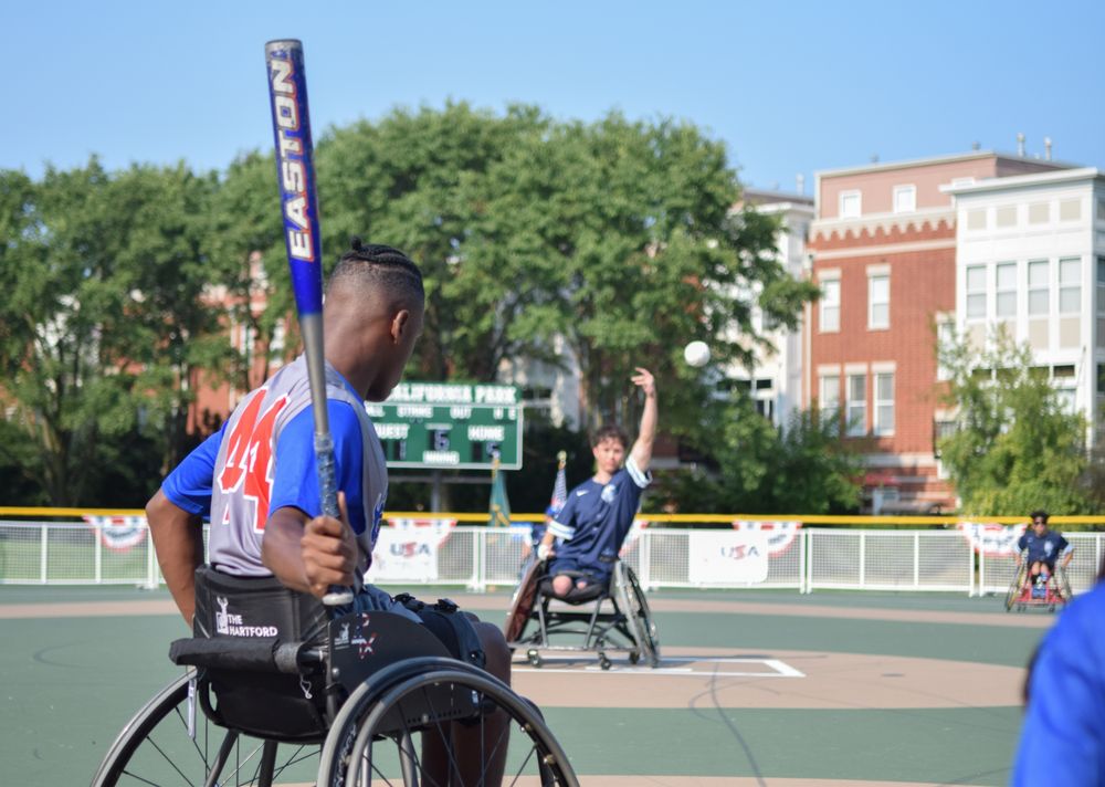 Mark, a player on the Chicago Junior Wheelchair Cubs wearing a grey jersey with blue sleeves and red lettering, waits an incoming pitch during the 2025 Wheelchair Softball Junior World Series at California Park's paved baseball diamond on Saturday.