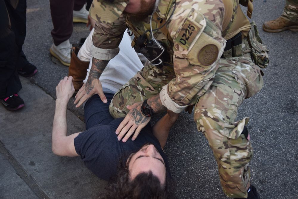 A federal agent in camouflage puts his knee on a man's sternum as he detains him in a navy-colored shirt Friday in the 3200 block of West Lawrence Avenue.