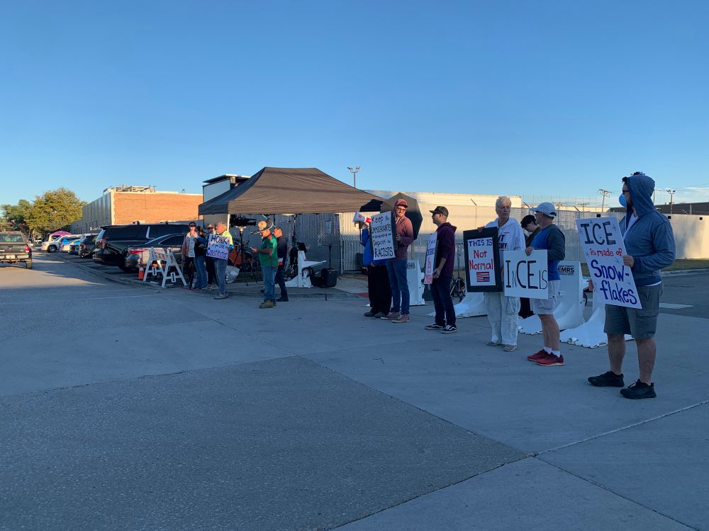 Several people standing in a line with signs bearing anti-ICE slogans like “ICE is made of snowflakes”