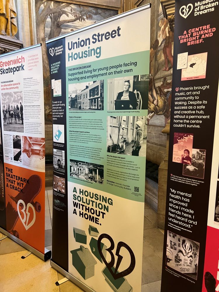 A standing banner in the Museum of Broken Dreams detailing the story of the Union Street housing project which aimed to deliver supported living for young people facing housing and employment on their own. The subtitle reads: 'A housing solution without a home'. Either side are other communities' stories of their projects which have failed to launch or been lost due to the lack of trust, investment, support and empowerment of community-led change.