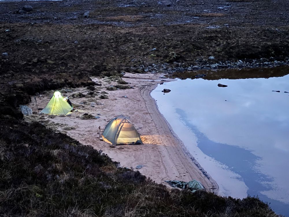 Two tents pitched on the sand by the water.