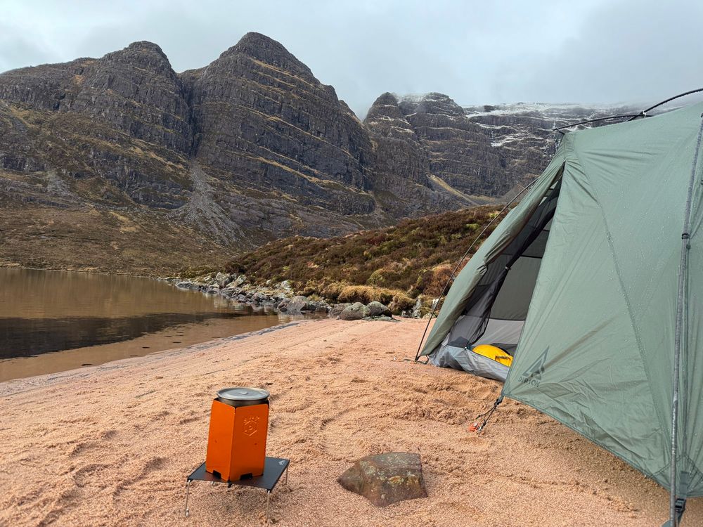 Tent pitched on a beach under mountain crags
