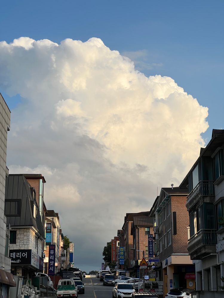 주택가 언덕길 너머 보이는 하늘에 솟아오르는 커다란 구름이 보인다.