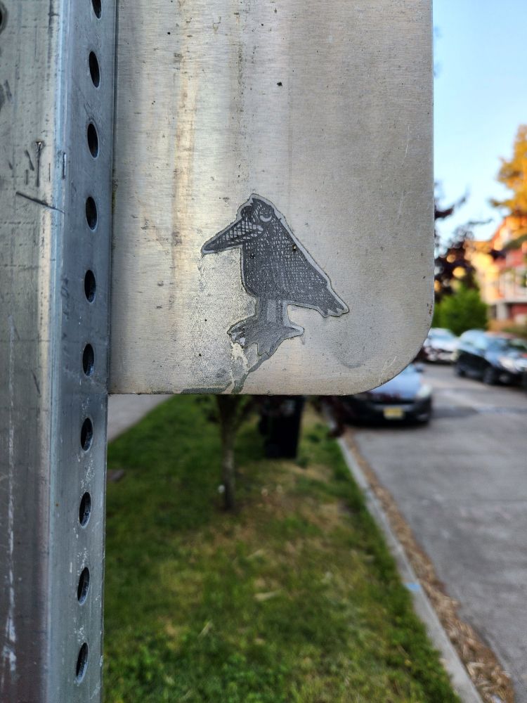 A worn, grimy sticker of a crow on a street sign