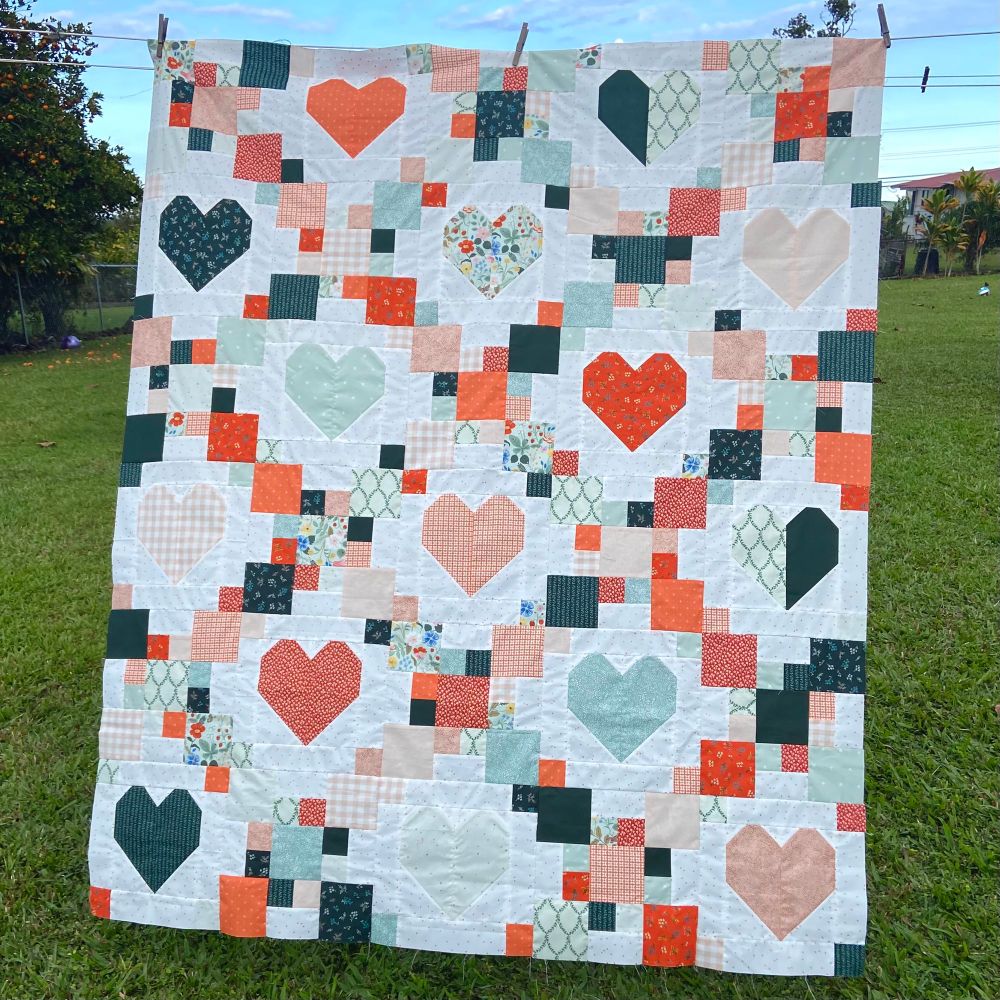 Green, red and white heart quilt hanging on display outside. 