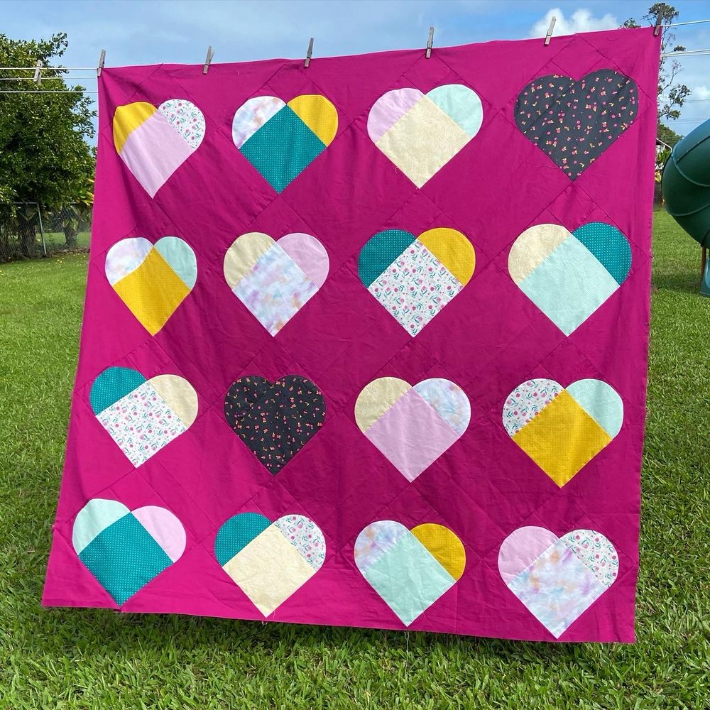 A large quilt with a pink background and multicolored hearts is displayed. 
