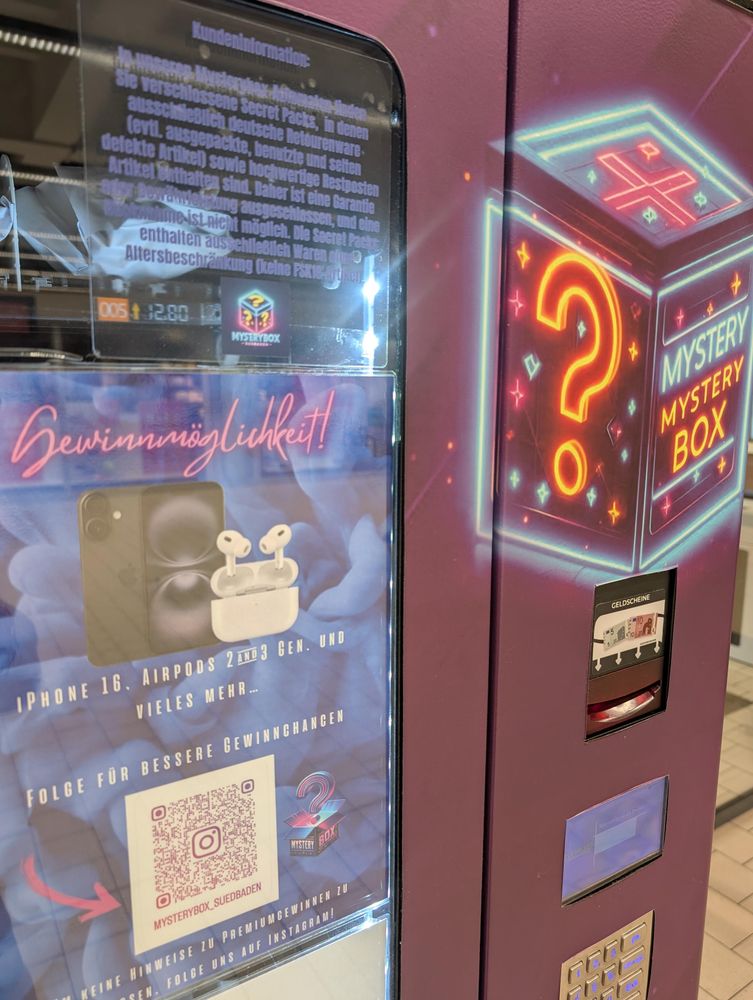 Mystery-Box-Automat in lila mit leuchtendem Fragezeichen, Werbung für Preise wie iPhone und AirPods, QR-Code und Geldschlitz sichtbar.
