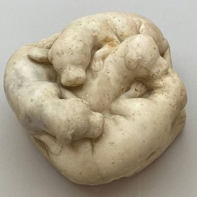 A small marble statue carved to resemble a circle of four dogs in a gently slumbering pile.