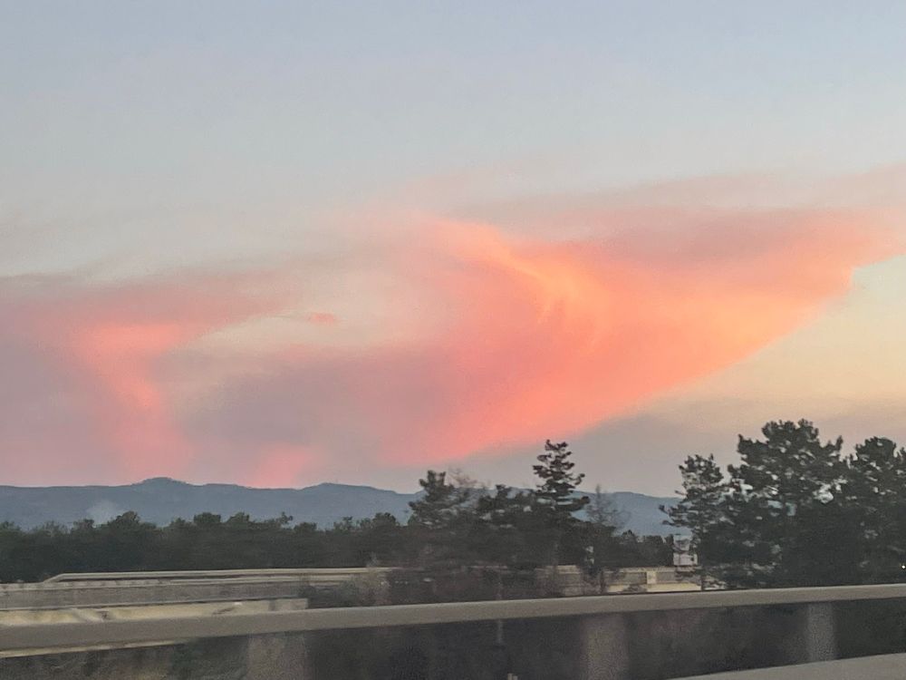 Orangerote Wolke, die einem Wirbel ähnelt über grünen Bäumen und der  Betonbegrenzung der Autobahn. 