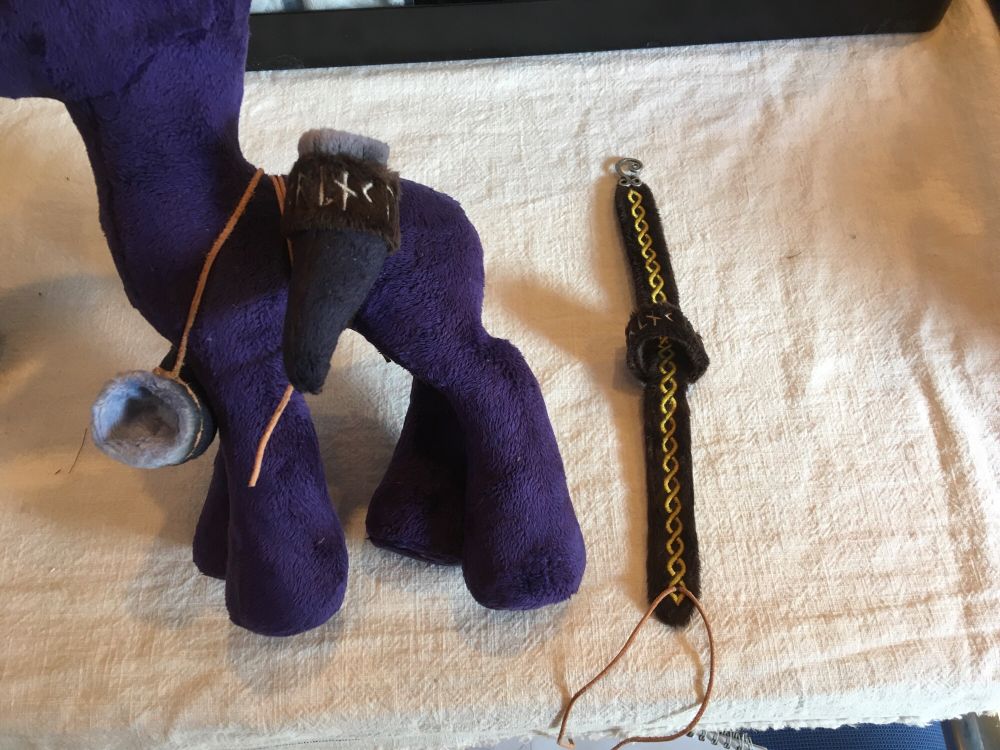 A bald plushie wearing an embroidered plush belt