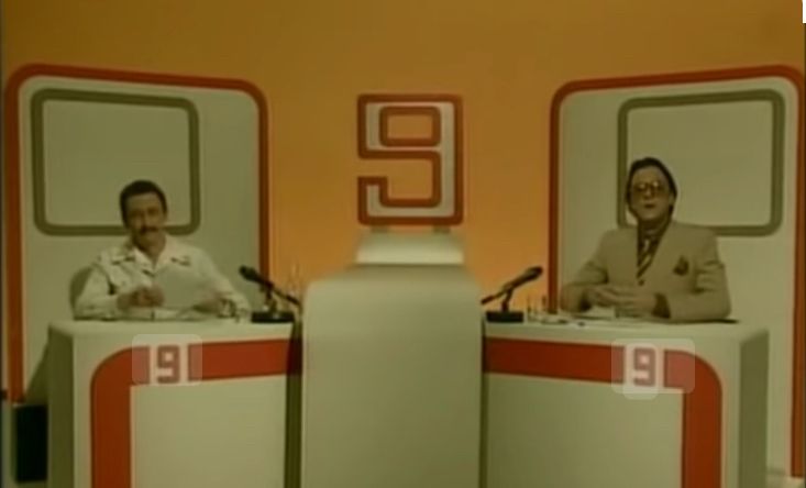 The Fast Show Channel 9 news - a 1990’s BBC comedy show. Two men sit at a very strange ‘foreign’ news desk.