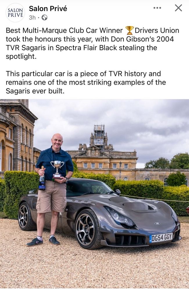 A man resembling a pink Shrek stands in front of a TVR. The mans face is split in two with a grin of absolute disbelief, whilst holding a magnum of champagne and a cup. He’s wearing a blue shirt and tan shorts, with green and pink converse shoes. The car is low and small, a brooding menace with a strange multicoloured grey… The car is in front of Blenheim Palace with manicured hedges. 