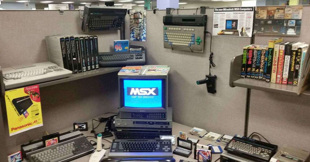 Bloop's MSX corner, featuring several machines and software placed about in the corner of an office cubicle. The Philips NMS8245 (left) is powered on and booting, connected to the monitor in the center.
